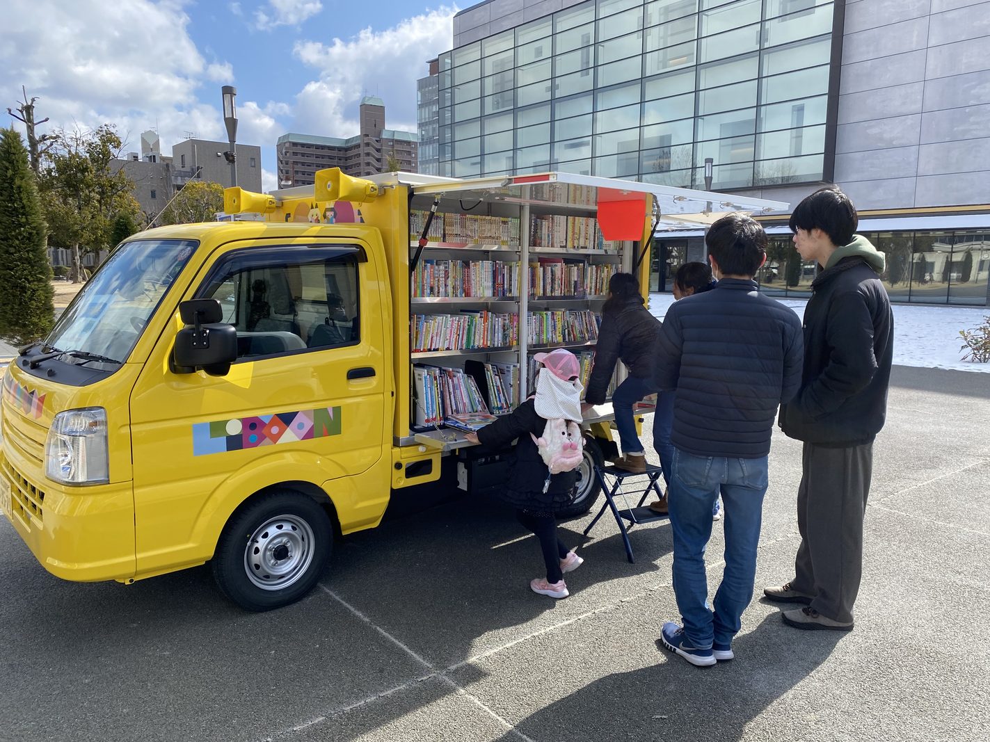 移動図書館「としょまる」。本を積んだ黄色い車の前で来場者が本を選ぶ様子